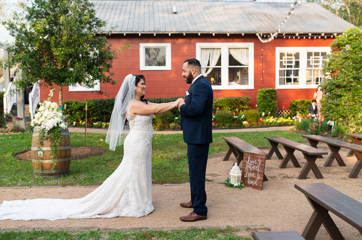 Elopement-4-1 A bride and groom stand together in front of a rustic red barn, smiling and embracing their wedding day.
