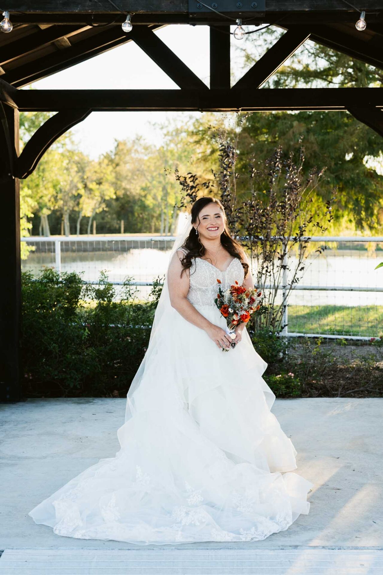 Andreea holds her bouquet beneath the gazebo with the ranch pond behind her.
