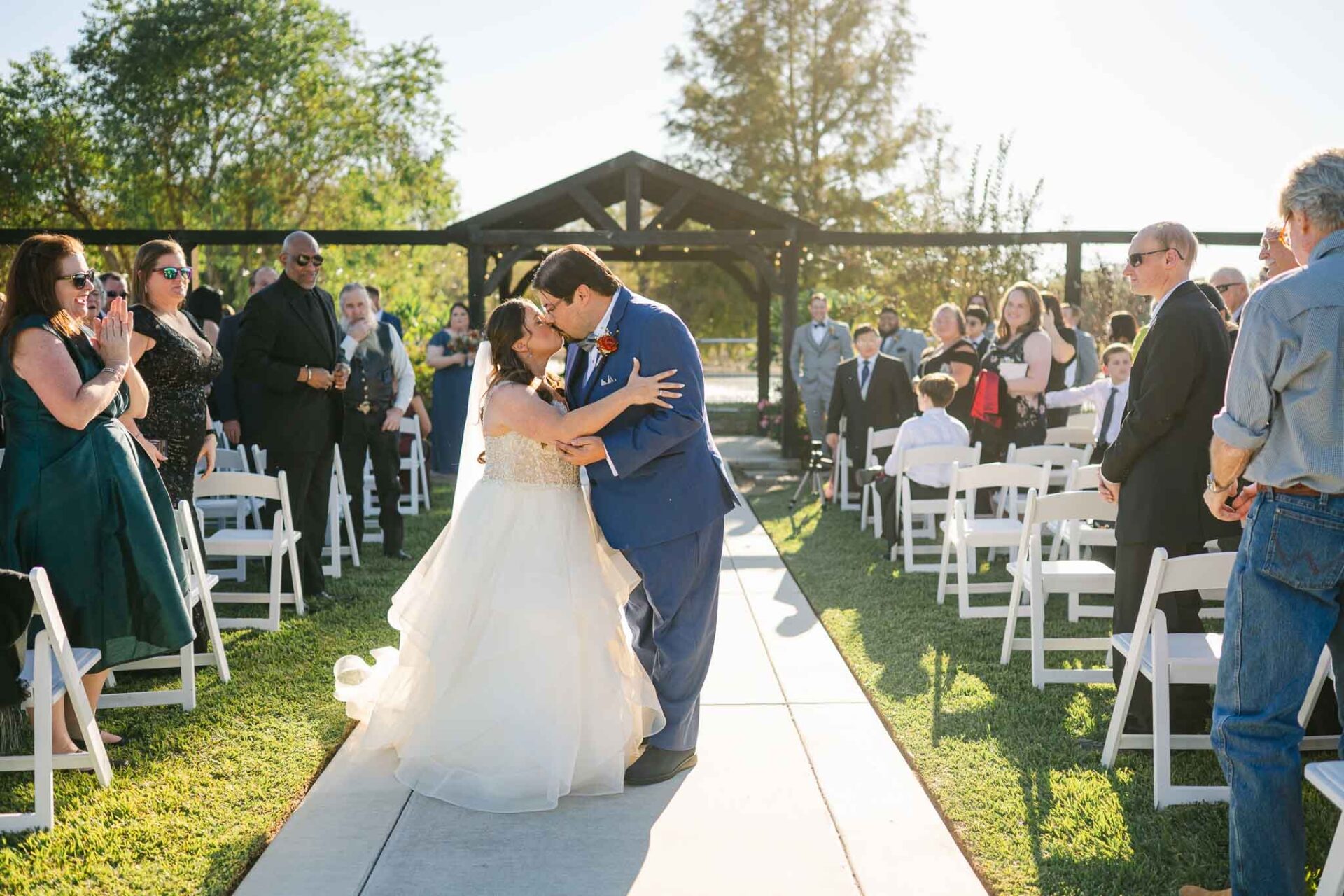 Andreea and Ram kiss beneath the gazebo as their guests watch from the garden ceremony.