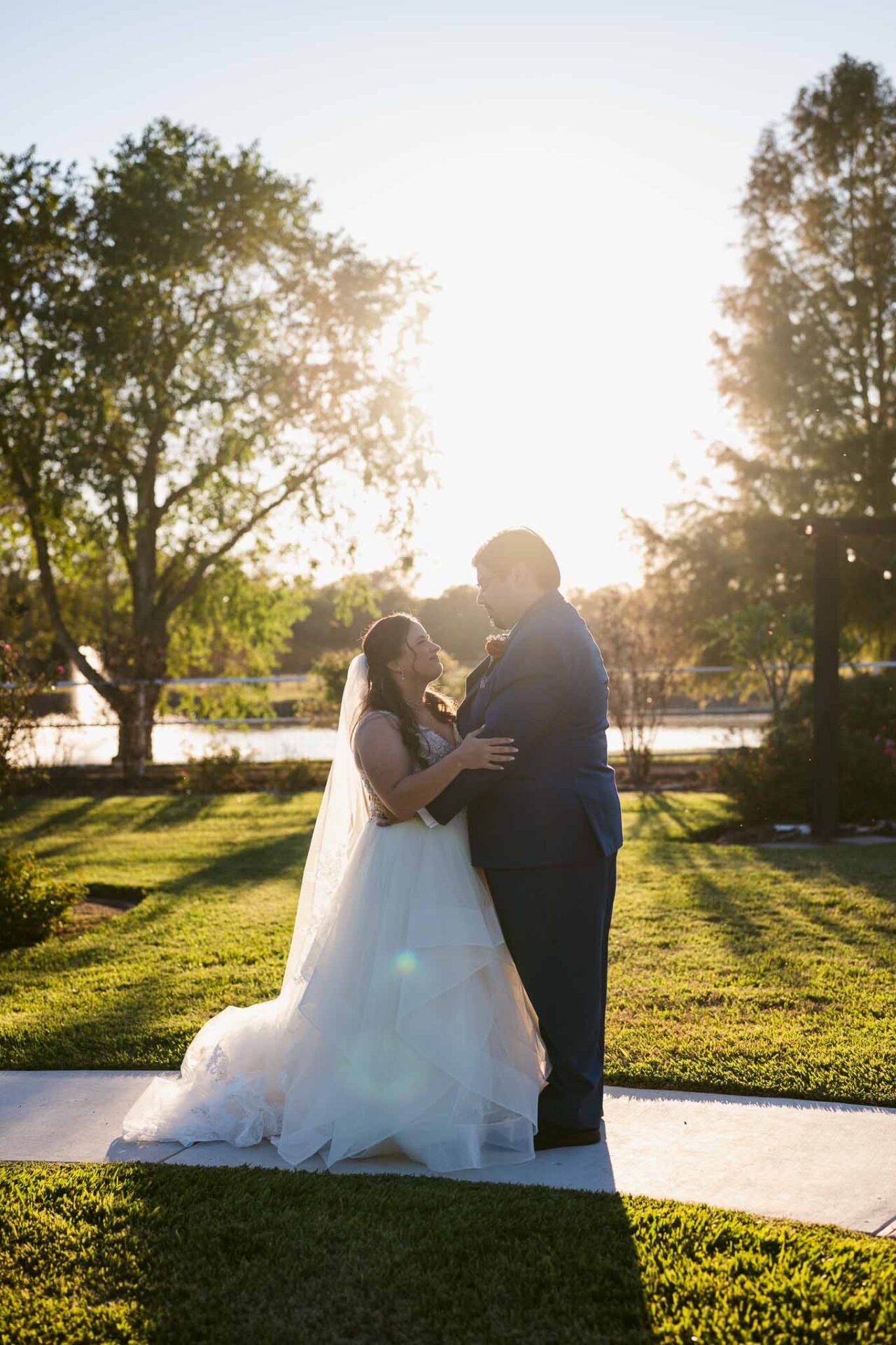 Andreea and Ram embrace in the sunset light beside the water.