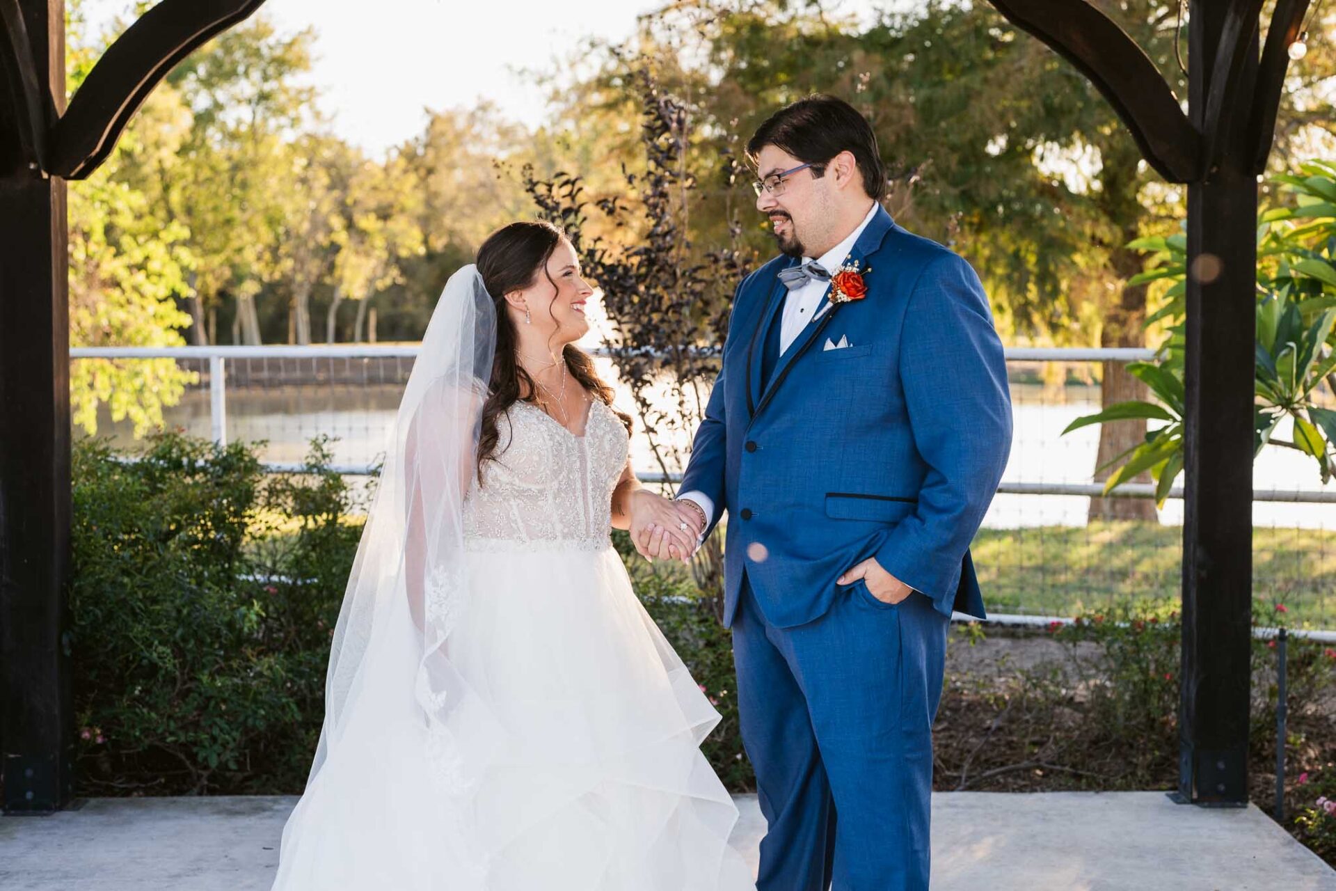 Andreea and Ram smile together beneath the timber gazebo beside the pond.