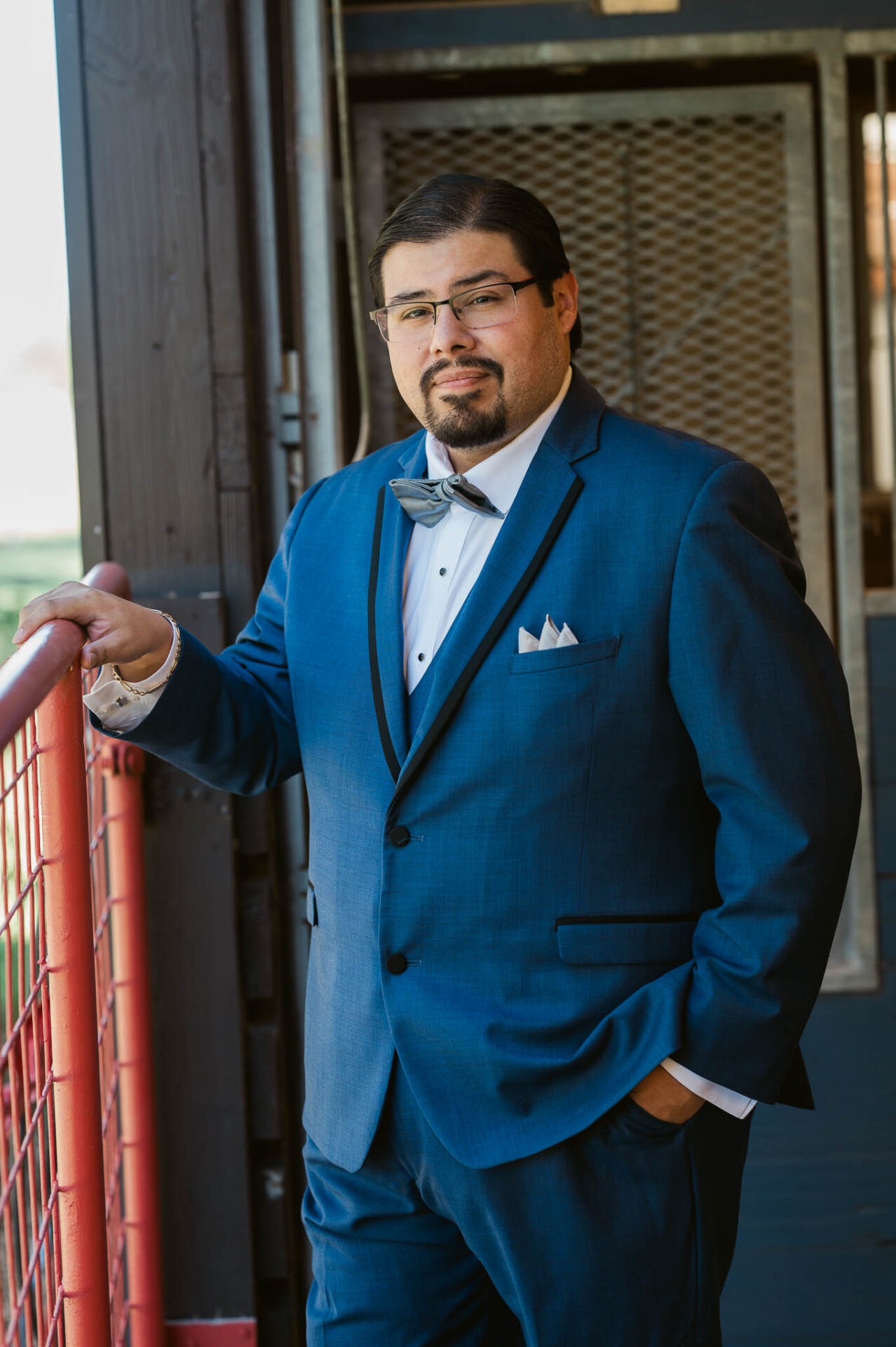Ram in his blue wedding suit beside a red ranch fence.