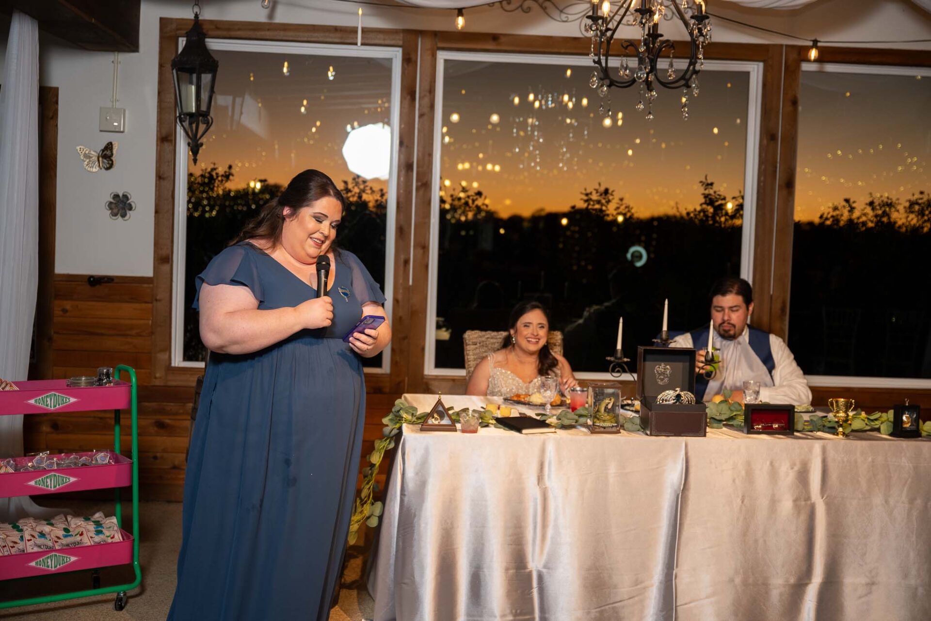 A bridesmaid gives a reception toast while Andreea and Ram listen.