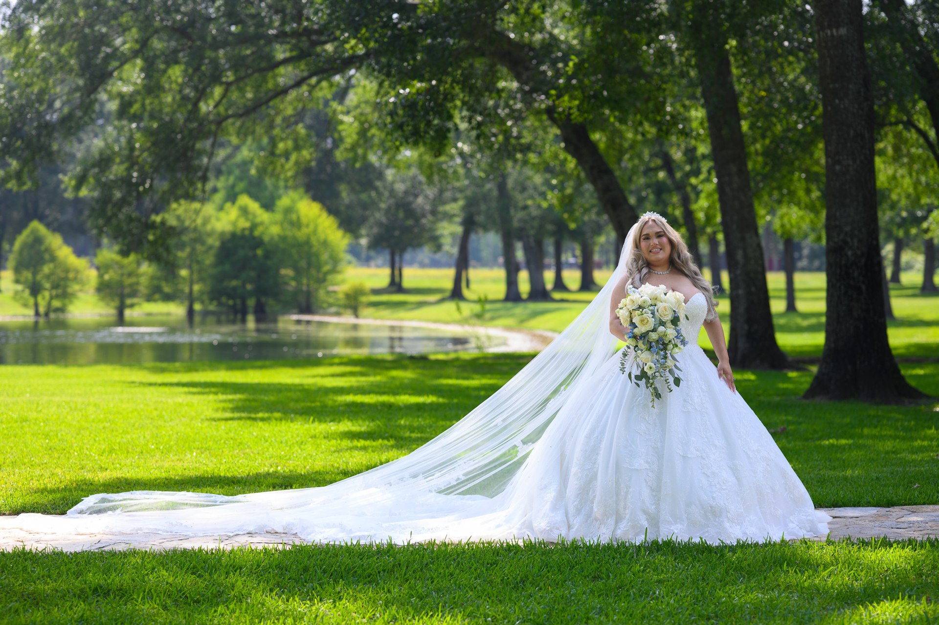 Marissa with her lace train spread across the grass beside the pond