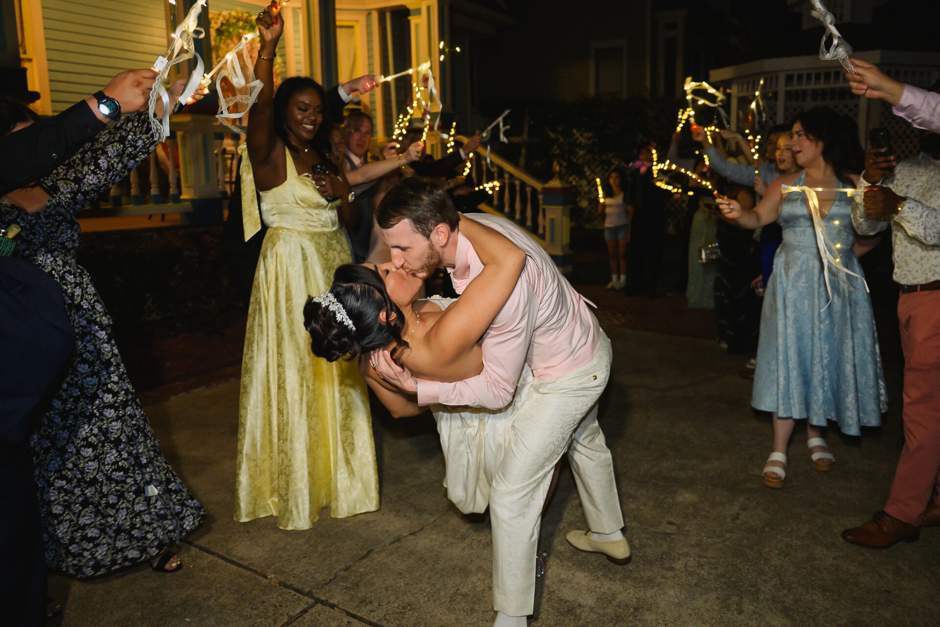 Zachary dipping Grisel for a kiss beneath guests’ glowing ribbon wands