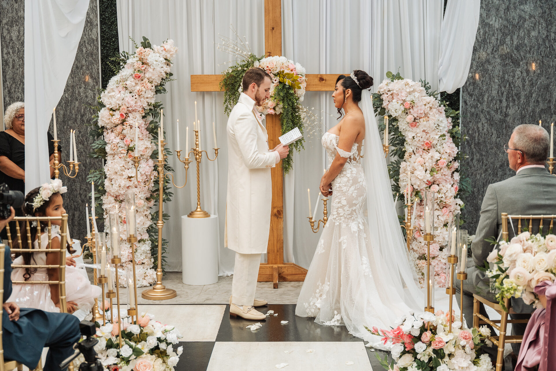 Zachary reading his vows to Grisel between blush floral arrangements