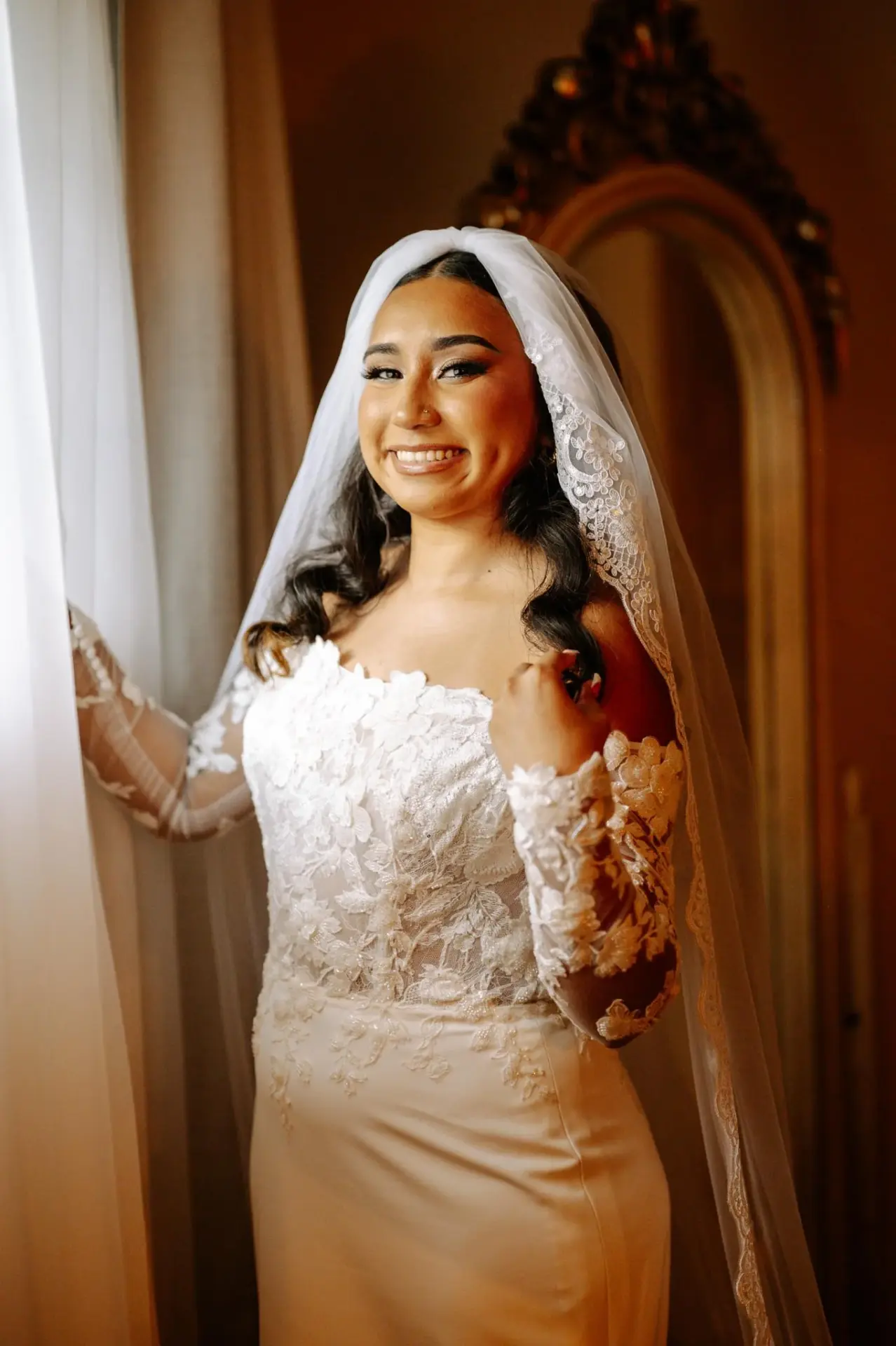 Vanessa in her lace wedding gown beside a sunlit window