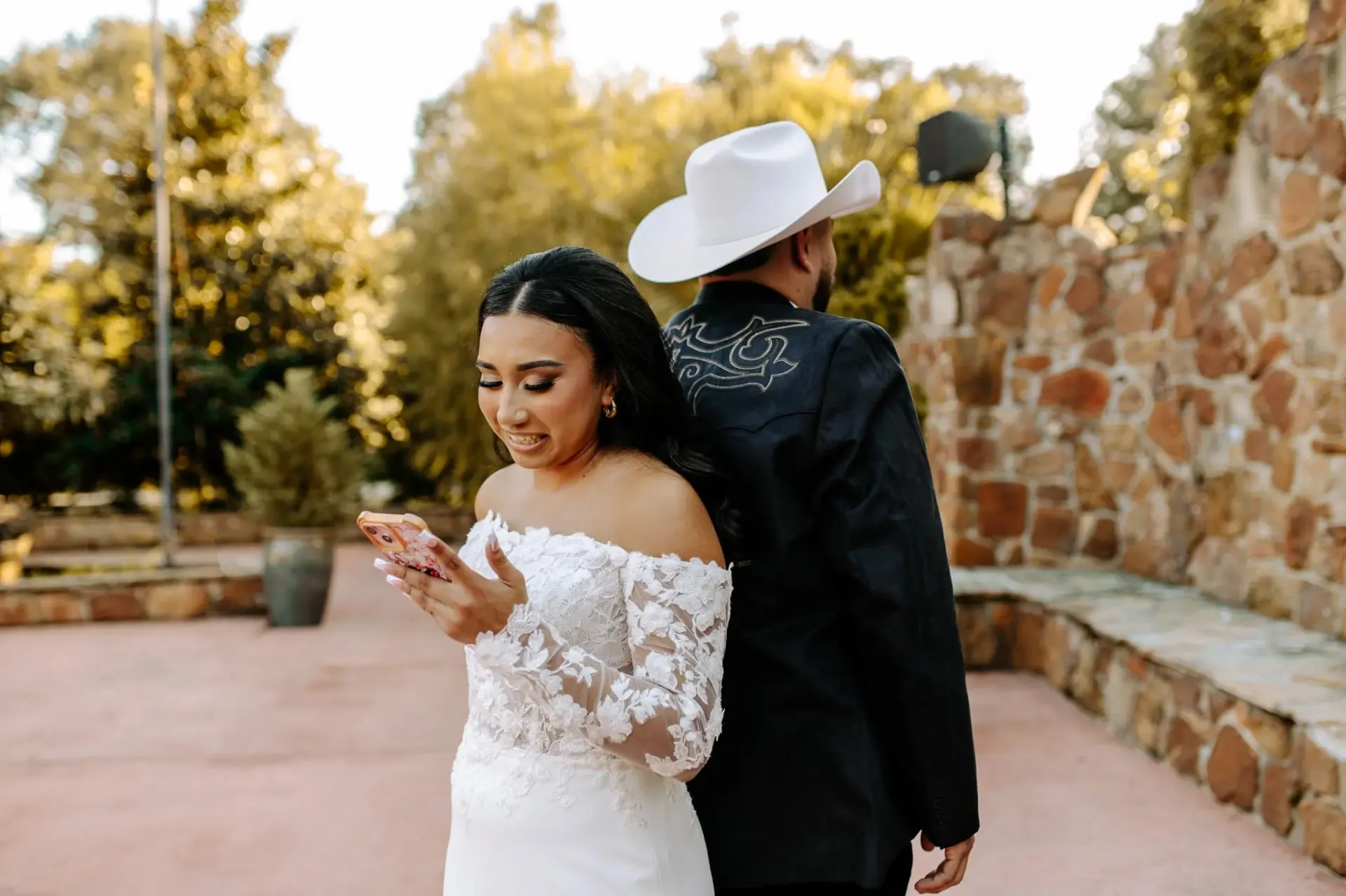 Vanessa and Reymundo standing back to back beside the stone wall