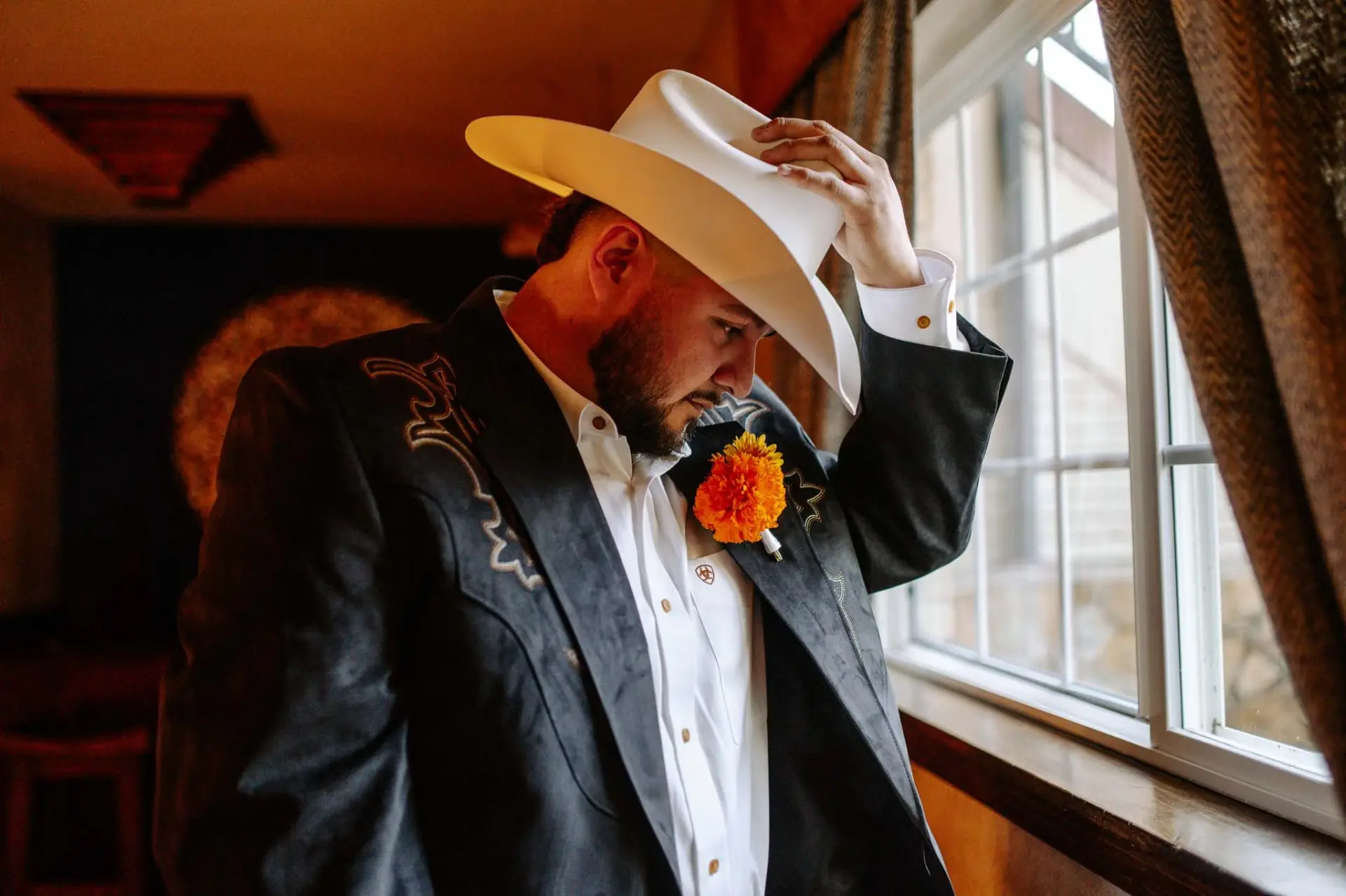Reymundo adjusting his white cowboy hat beside a window