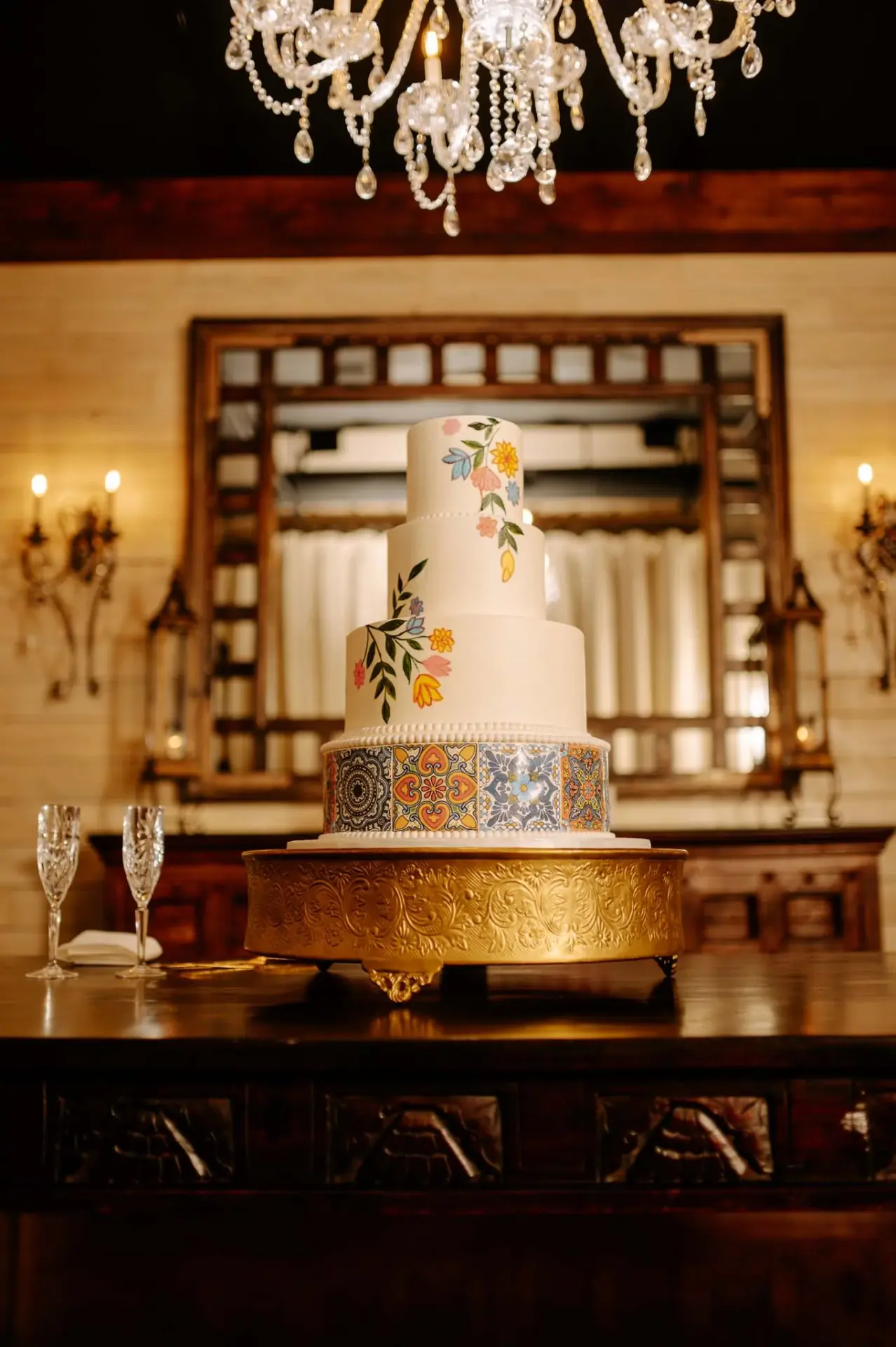 Wedding cake displayed beneath a chandelier against carved wood