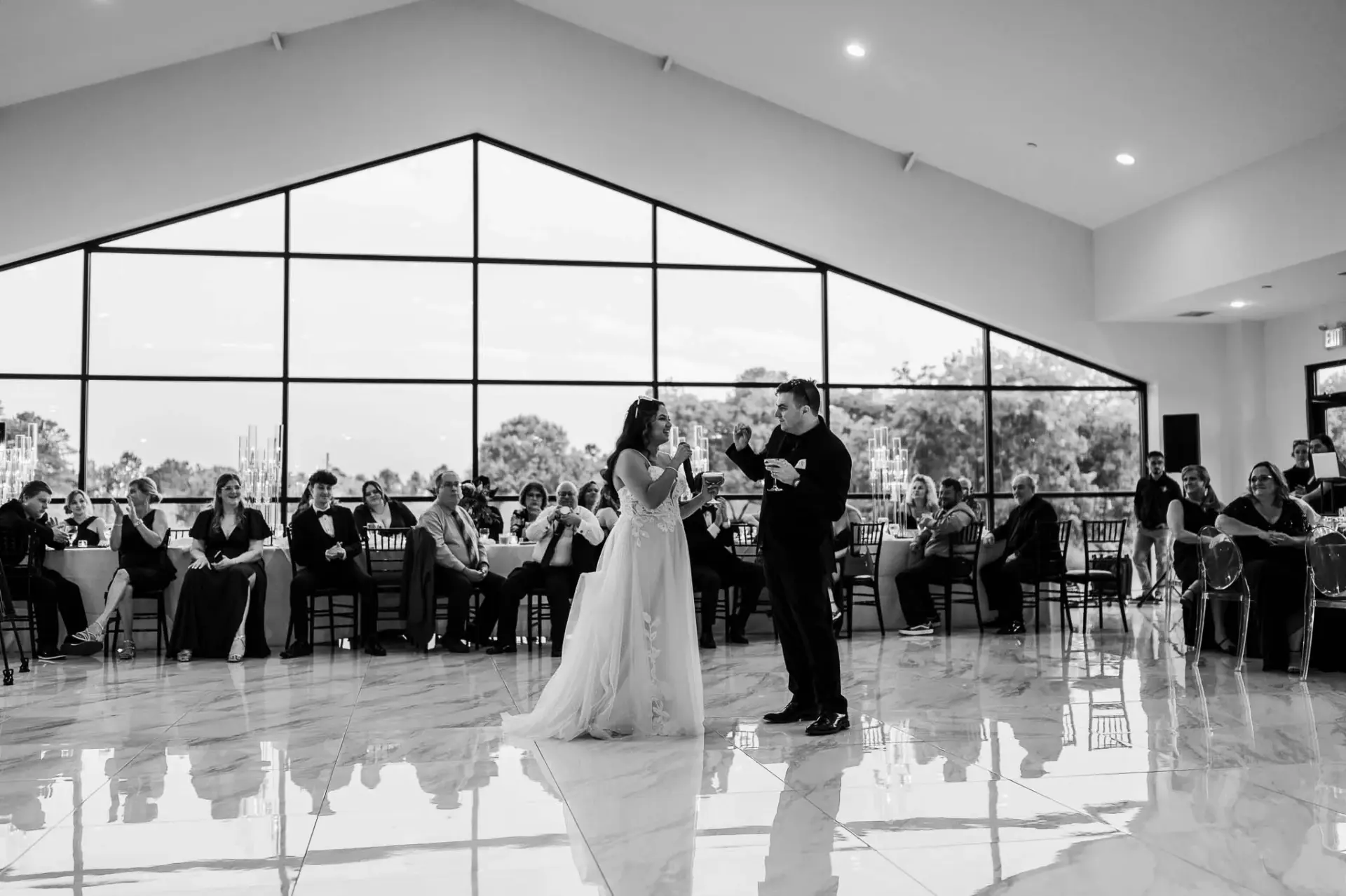 Black-and-white wide view of Kyle and Lauren’s ceremony inside the glass-fronted venue