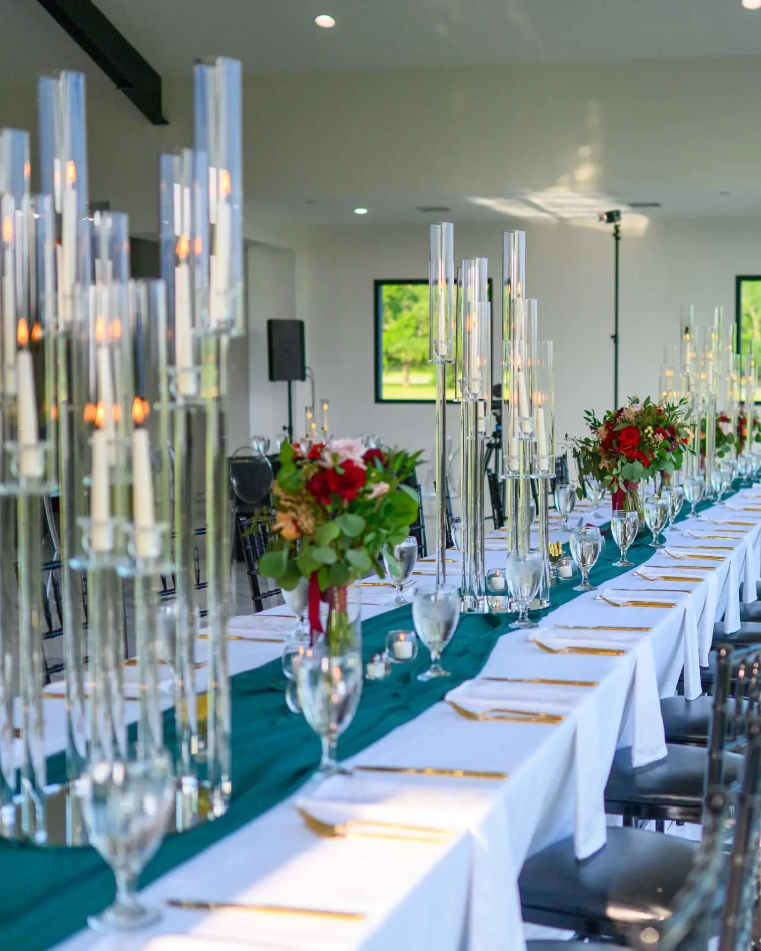 Long reception table set with glassware, candles, and red floral arrangements