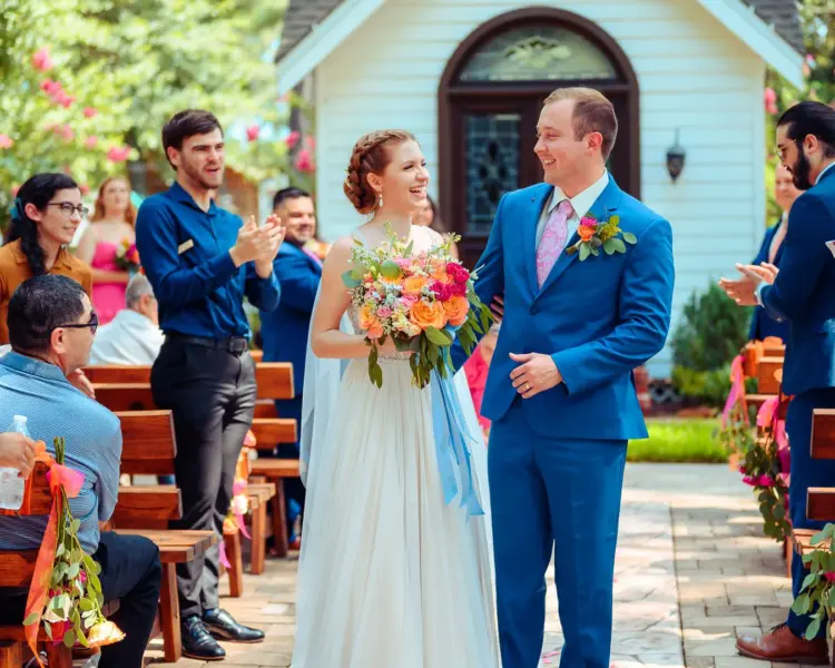 A couple exchanging vows in a charming chapel, surrounded by floral arrangements and seated guests witnessing the ceremony.