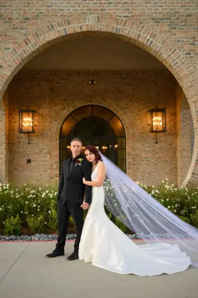 Bride and groom standing together at a rustic ranch, surrounded by greenery and wooden structures, smiling joyfully.