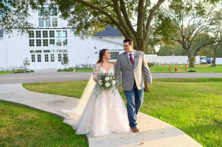 Bride and groom walk down a charming path at a barn, radiating happiness amidst a picturesque outdoor setting.